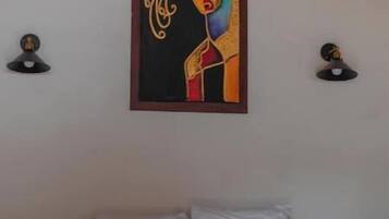 Een slaapkamer met een bed, een kunstwerk in een lijst erboven en twee wandlampen.