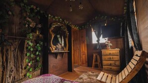 A rustic bedroom with a wooden bed, a wooden chair, a dresser, and a mirror.
