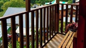 A wooden balcony with a view of a green hillside and buildings.