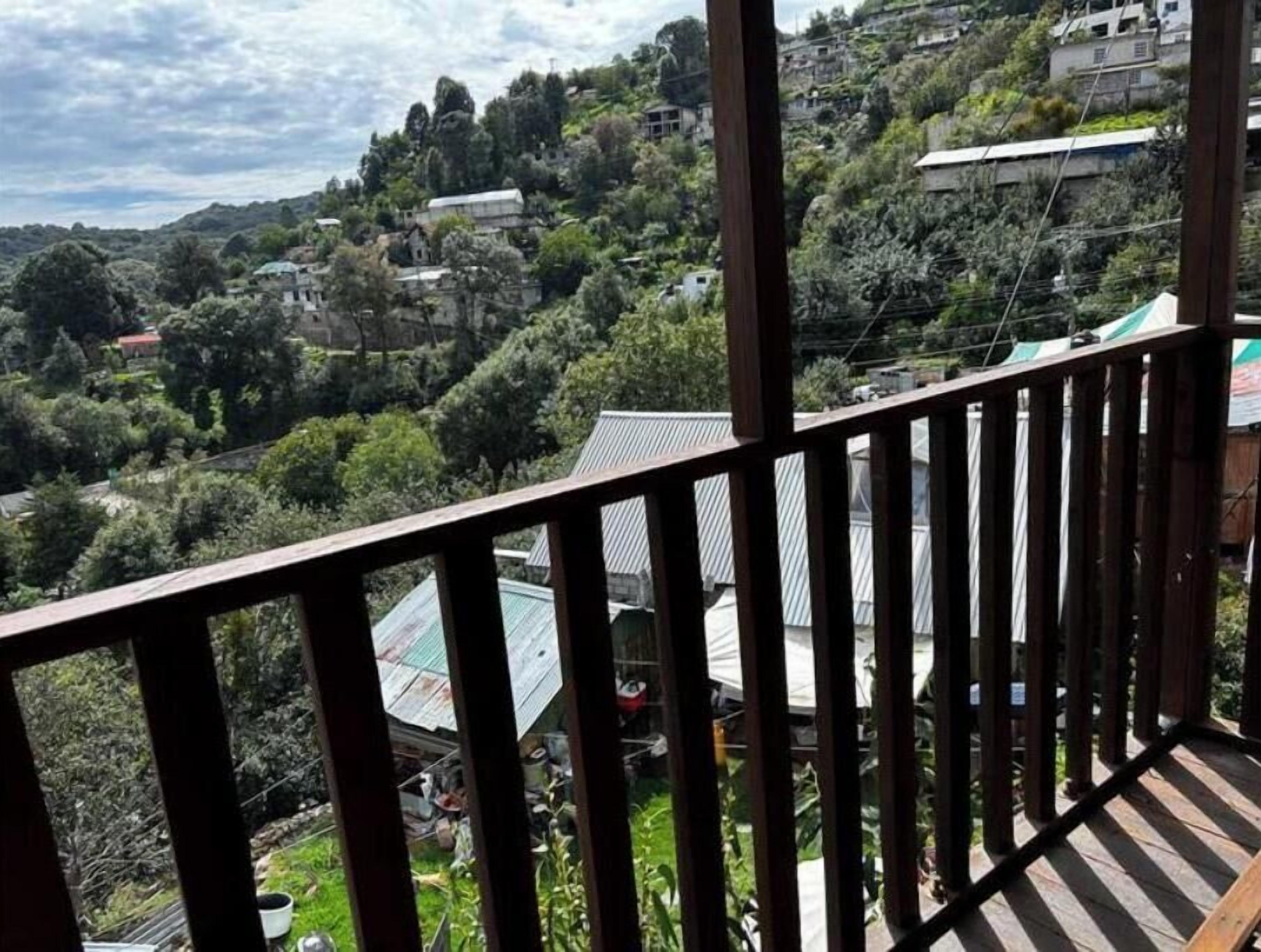 Vista da un balcone su una collina con case e vegetazione.
