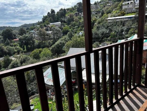 Vista desde un balcón con vistas a una colina con casas y vegetación.
