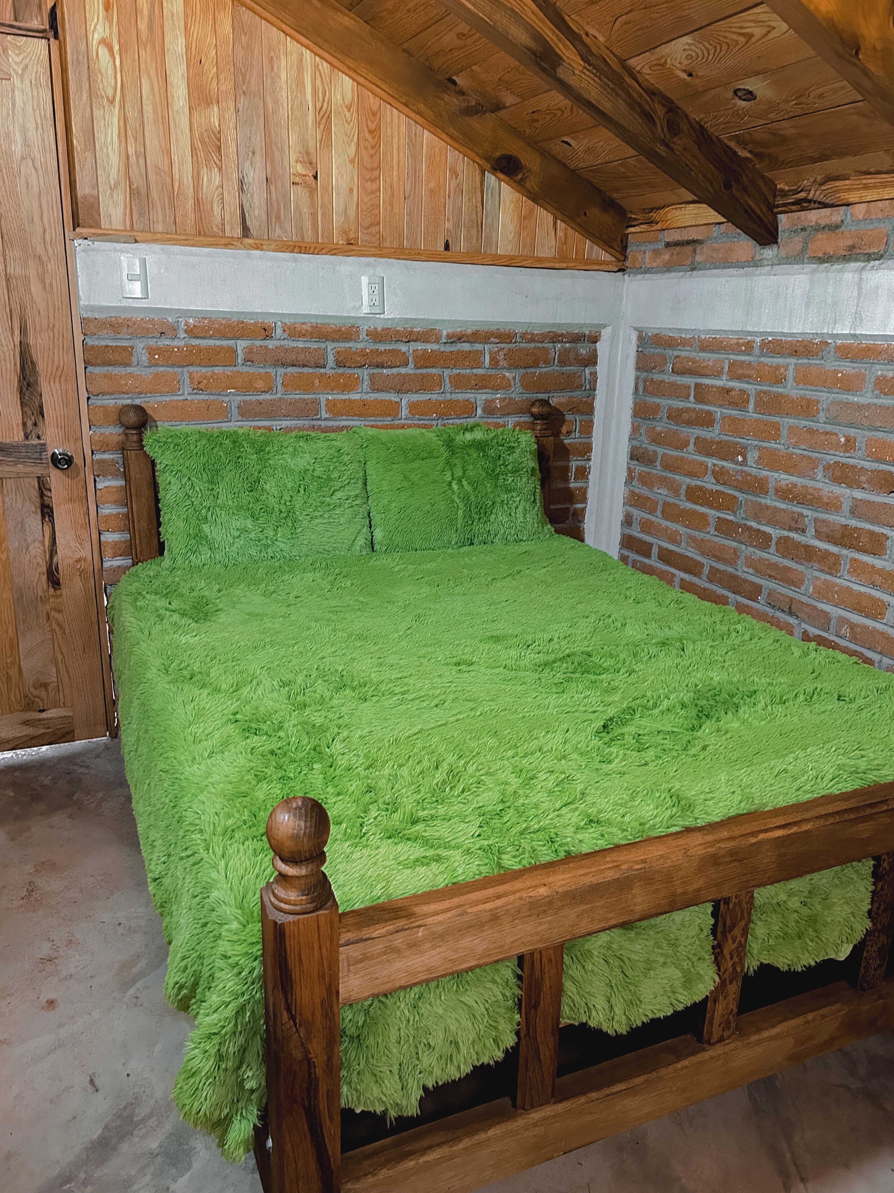 Une pièce avec un lit en bois, une literie verte, des murs en briques et un plafond en bois.