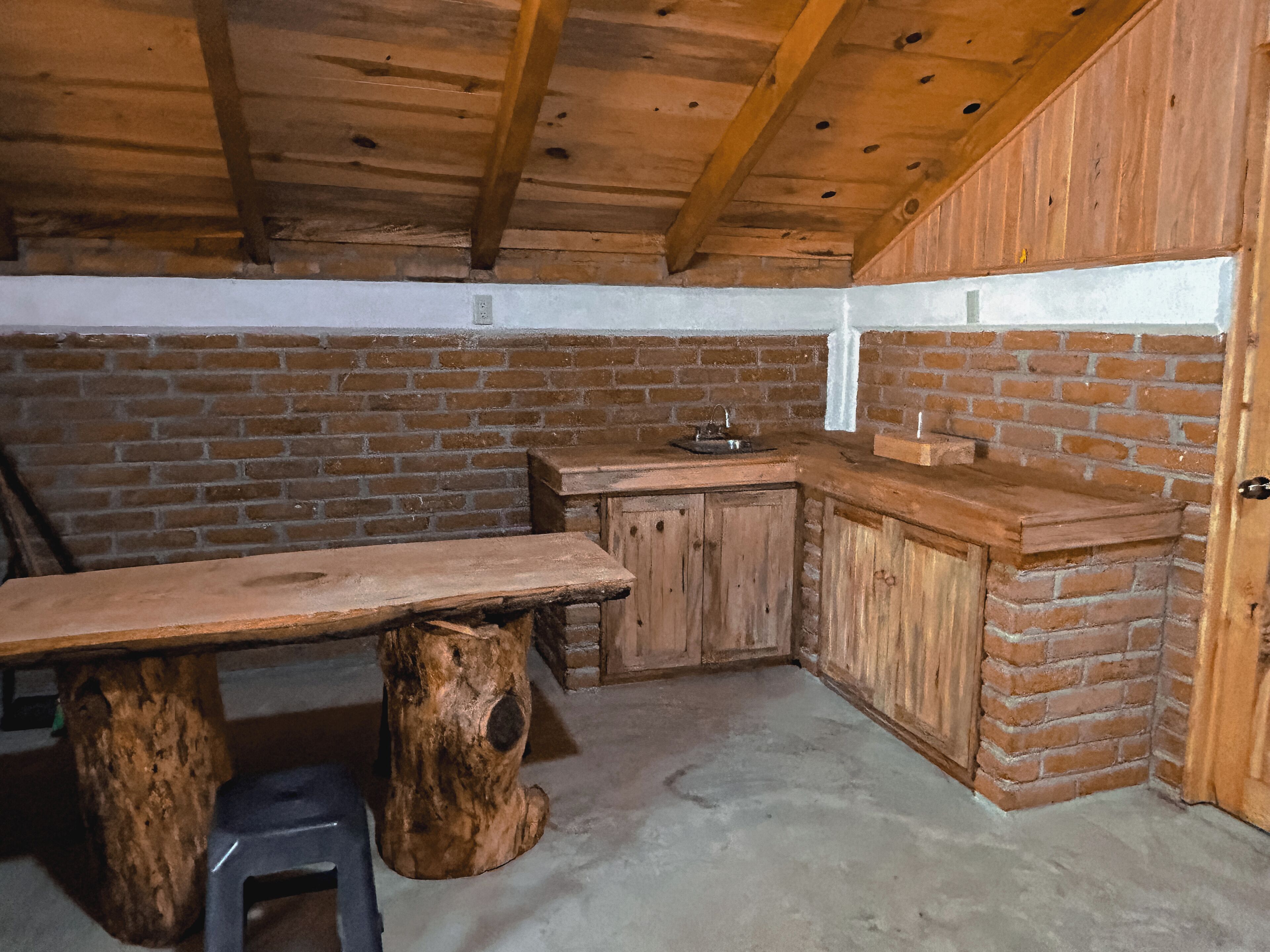 Une cuisine rustique avec une table en bois, des tabourets et un mur en briques.