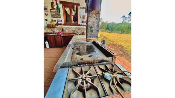 Una cocina rústica al aire libre con estufa a gas, pileta y encimera de madera.