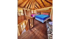 Una cabaña de madera con un dormitorio en el altillo, un balcón y una cama con colcha de diseño azul y blanco.