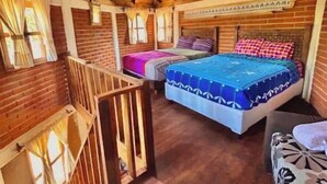 Una cabaña de madera con un dormitorio en el altillo, un balcón y una cama con colcha de diseño azul y blanco.