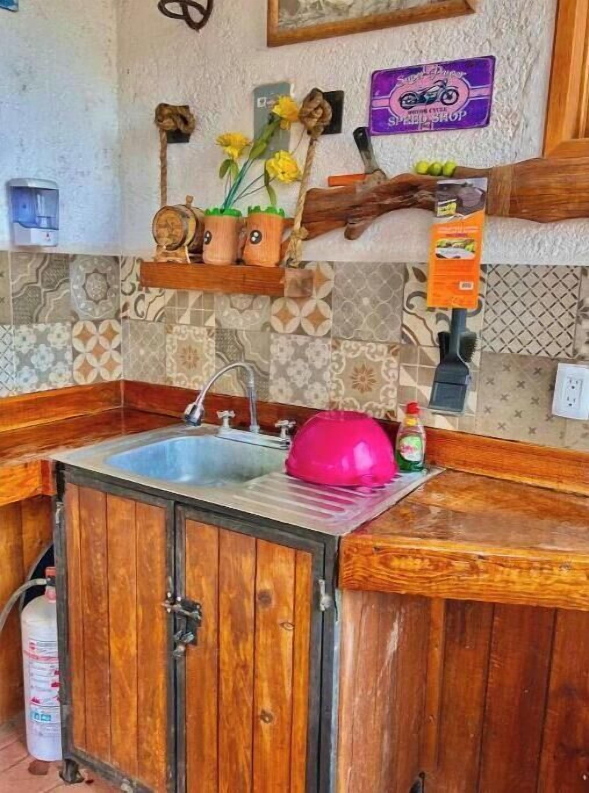 Une cuisine avec des meubles de rangement en bois, un évier et une étagère ornée d’objets décoratifs.