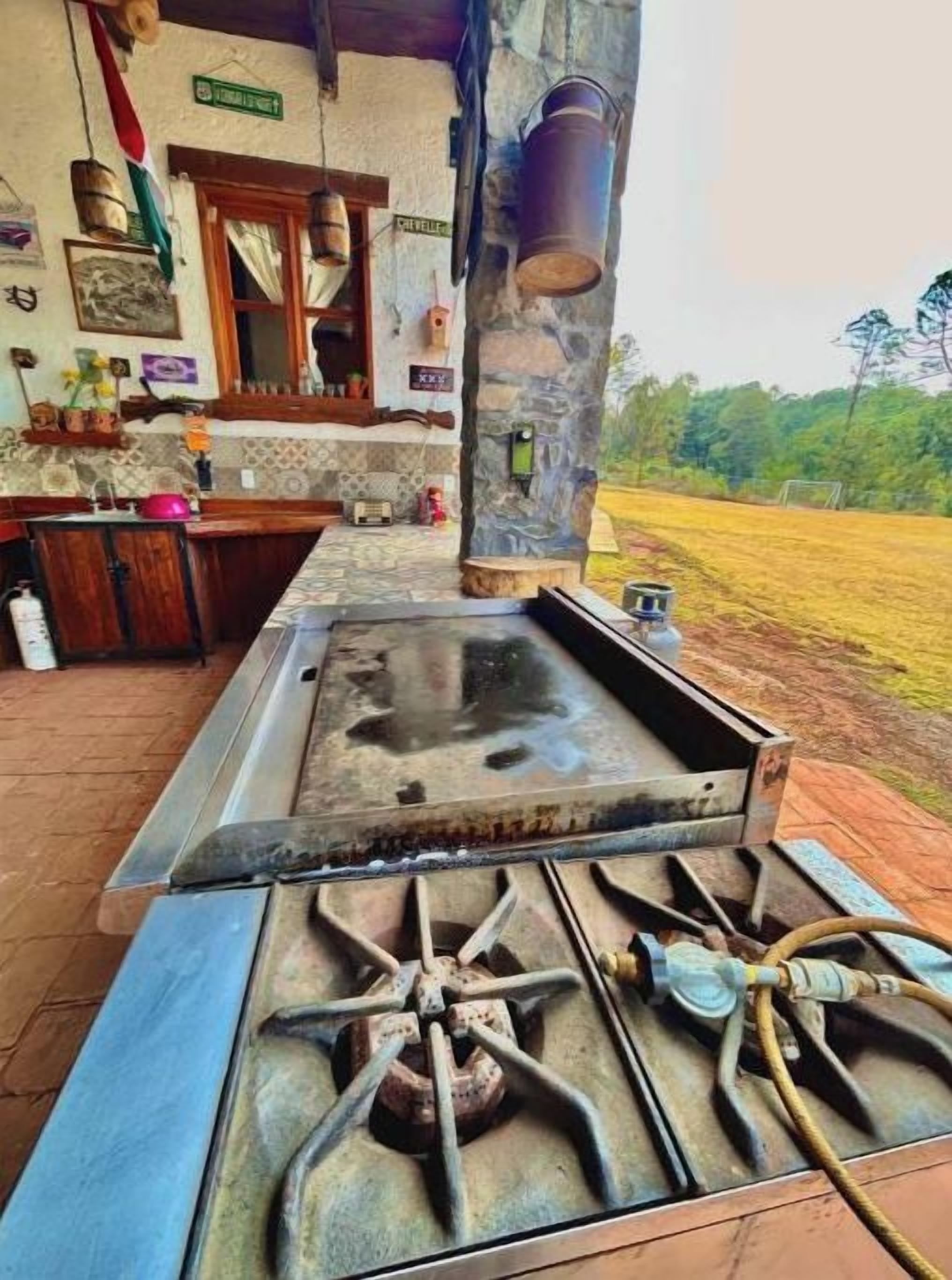 A rustic outdoor kitchen with a gas stove, a sink, and a wooden counter.