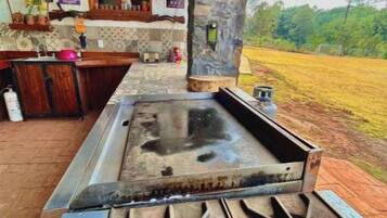 A rustic outdoor kitchen with a gas stove, a sink, and a wooden counter.