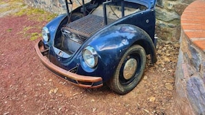 Un coche antiguo estacionado afuera, con un muro de piedra y un edificio de ladrillo al fondo.