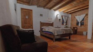 A bedroom with a wooden bed, a wooden bench, a tiled floor, and a brick wall.