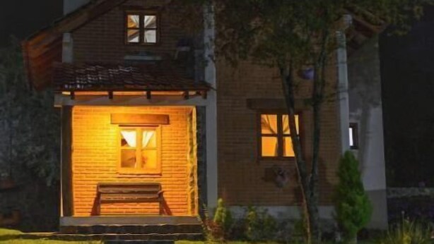 A two-story house with a wooden exterior, a front porch, and a small garden area.