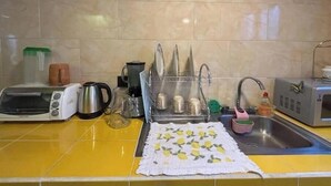 Une cuisine avec un plan de travail jaune, un grille-pain, une bouilloire, un mixeur, un égouttoir et un évier.