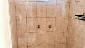 Un pequeño espacio de ducha con azulejos, dos llaves y una cortina.