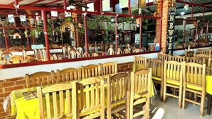 Interior de restaurante con sillas y mesas de madera, paredes de ladrillo y estructura de techo roja.