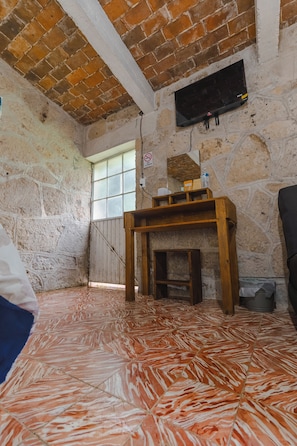 A room with a stone wall, a wooden table, a television mounted on the wall, and a window with a view.