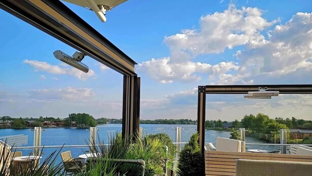A balcony with a view of a lake, outdoor seating, and a glass railing.