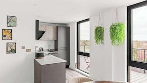 A modern kitchen with a central island, a dining area with a wooden table, and large windows with a view of the outside.