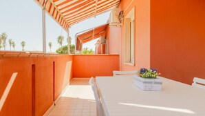 A balcony with a white table, a striped awning, and a potted plant.