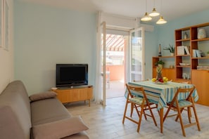 A living room with a sofa, TV, dining table with chairs, and a bookshelf.
