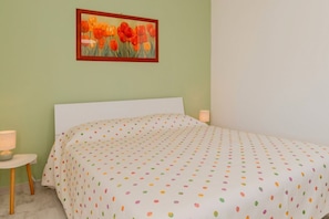 A bedroom with a bed, a nightstand, a lamp, and a framed painting on the wall.