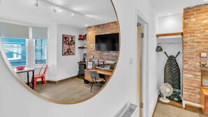 Une chambre moderne avec un grand miroir, un bureau, une chaise, une télévision et un mur en briques.