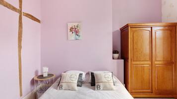 A bedroom with a bed, pillows, a wooden wardrobe, a small round table, and a wall-mounted painting.