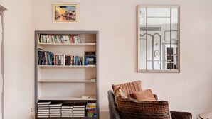 A living room with a bookshelf, a sofa with patterned cushions, a framed picture, and a mirror on the wall. - Apartment 'La Tourelle Des Cordeliers' with Private Terrace, Shared Garden and Wi-Fi (Loches)