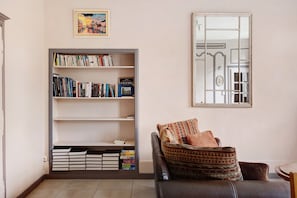 Un soggiorno con libreria, un divano con cuscini decorati, un quadro incorniciato e uno specchio a parete.