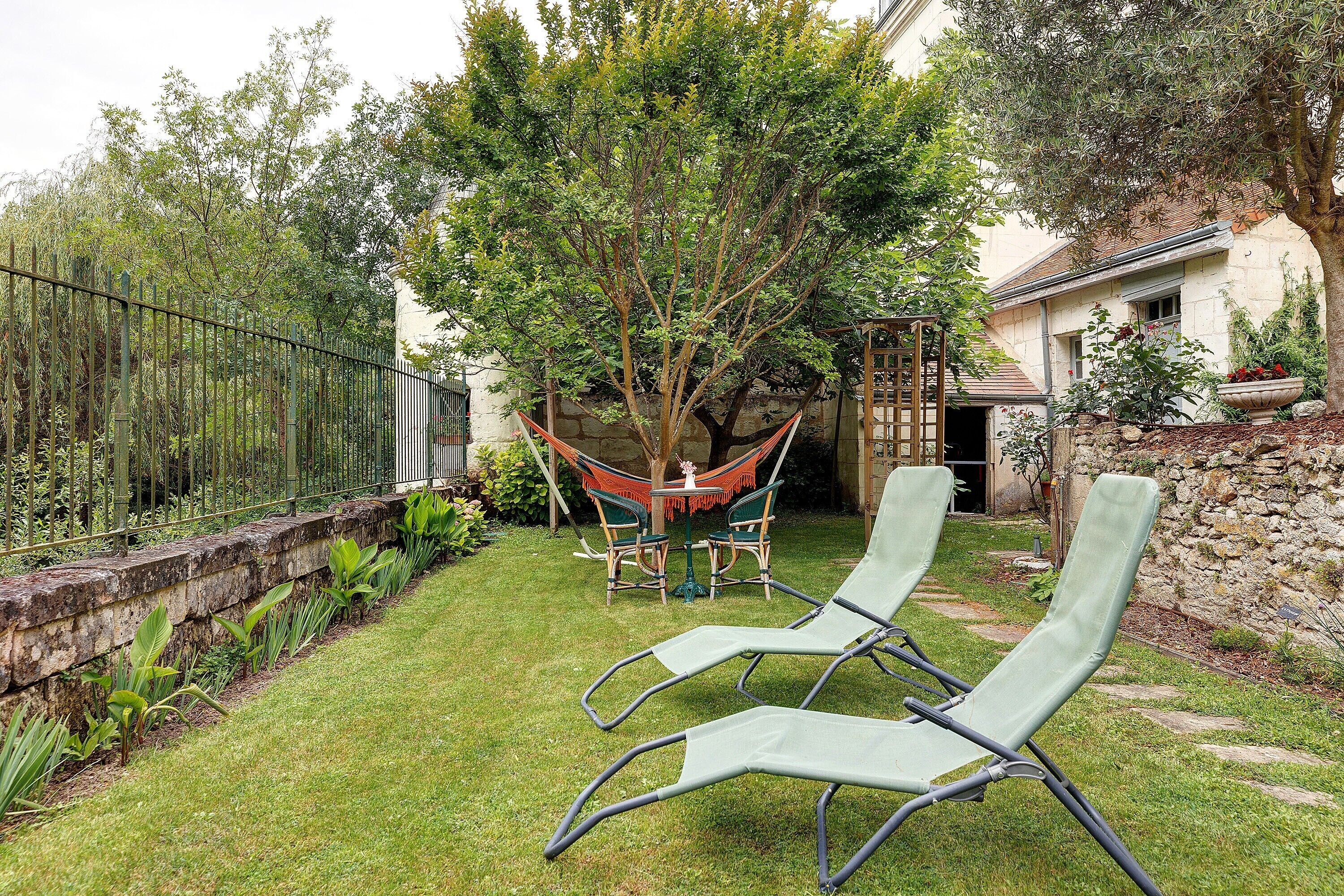 A backyard with a hammock, two lounge chairs, a stone wall, and a house in the background.