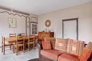 A dining area with a wooden table and chairs, a sofa with patterned cushions, a cabinet, and a wall-mounted mirror.