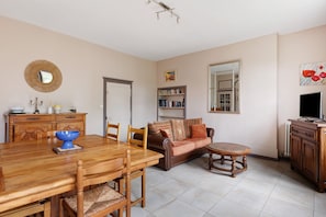 A dining area with a wooden table, chairs, a blue bowl, a sofa, a small round table, and a bookshelf.
