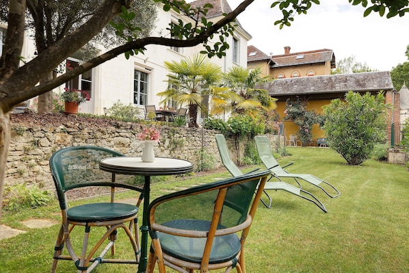 A garden with a stone wall, a white building, and a table with chairs.