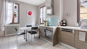 A modern kitchen with a white countertop, stainless steel appliances, and a dining area with a white table and chairs. - Apartment 'La Tourelle Des Cordeliers' with Private Terrace, Shared Garden and Wi-Fi (Loches)