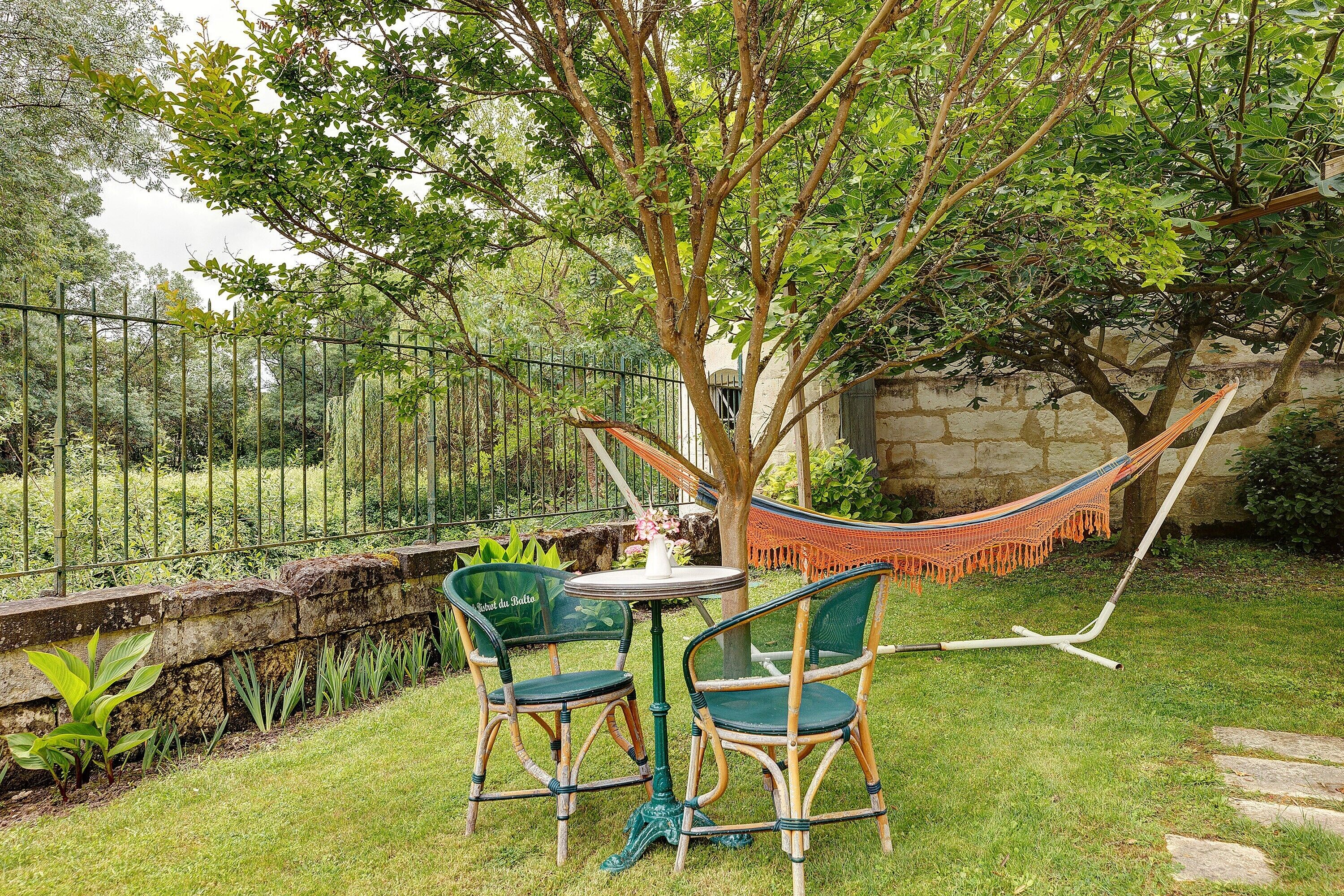 A garden with a table and chairs, a hammock, and a stone wall.