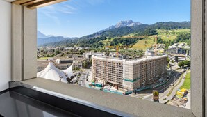 A view from a window overlooking a cityscape with a large building under construction, a McDonald's sign, and mountains in the background.