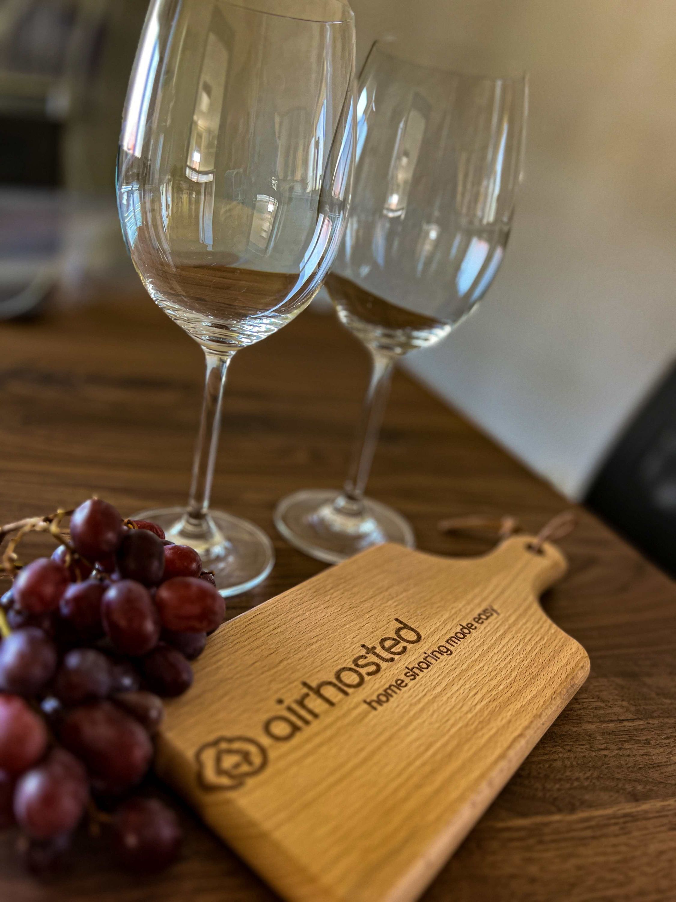 Dos copas de vino vacías sobre una mesa de madera con una tabla de cortar de madera que dice 'airhosted home sharing'.
