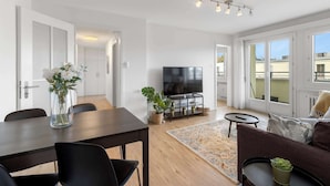 Ein modernes Wohnzimmer mit Esstisch, Stühlen, Fernseher und einer Couch.