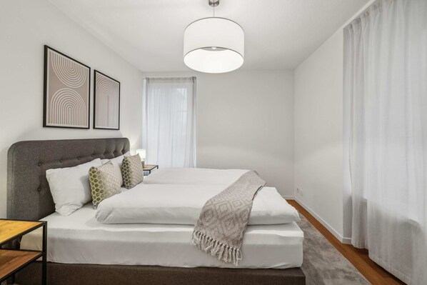 A modern bedroom with a large bed, a grey headboard, and a hanging light fixture. - Modern 2 BDR-flat  top location (Kriens)