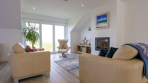 Un soggiorno moderno con due divani beige, una grande finestra, una pianta e un televisore su un mobile in legno.