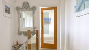 Un corridoio con ringhiera in vetro, una porta in legno e uno specchio incorniciato al muro.