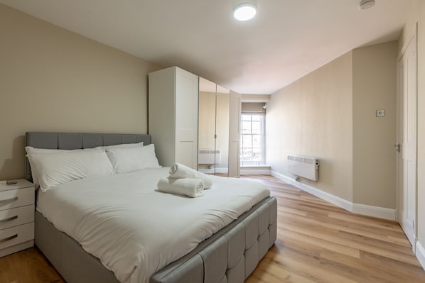 A bedroom with a large bed, a nightstand, a wardrobe, and a radiator.