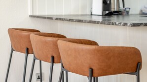 A kitchen area with a countertop, a coffee maker, and three brown chairs.