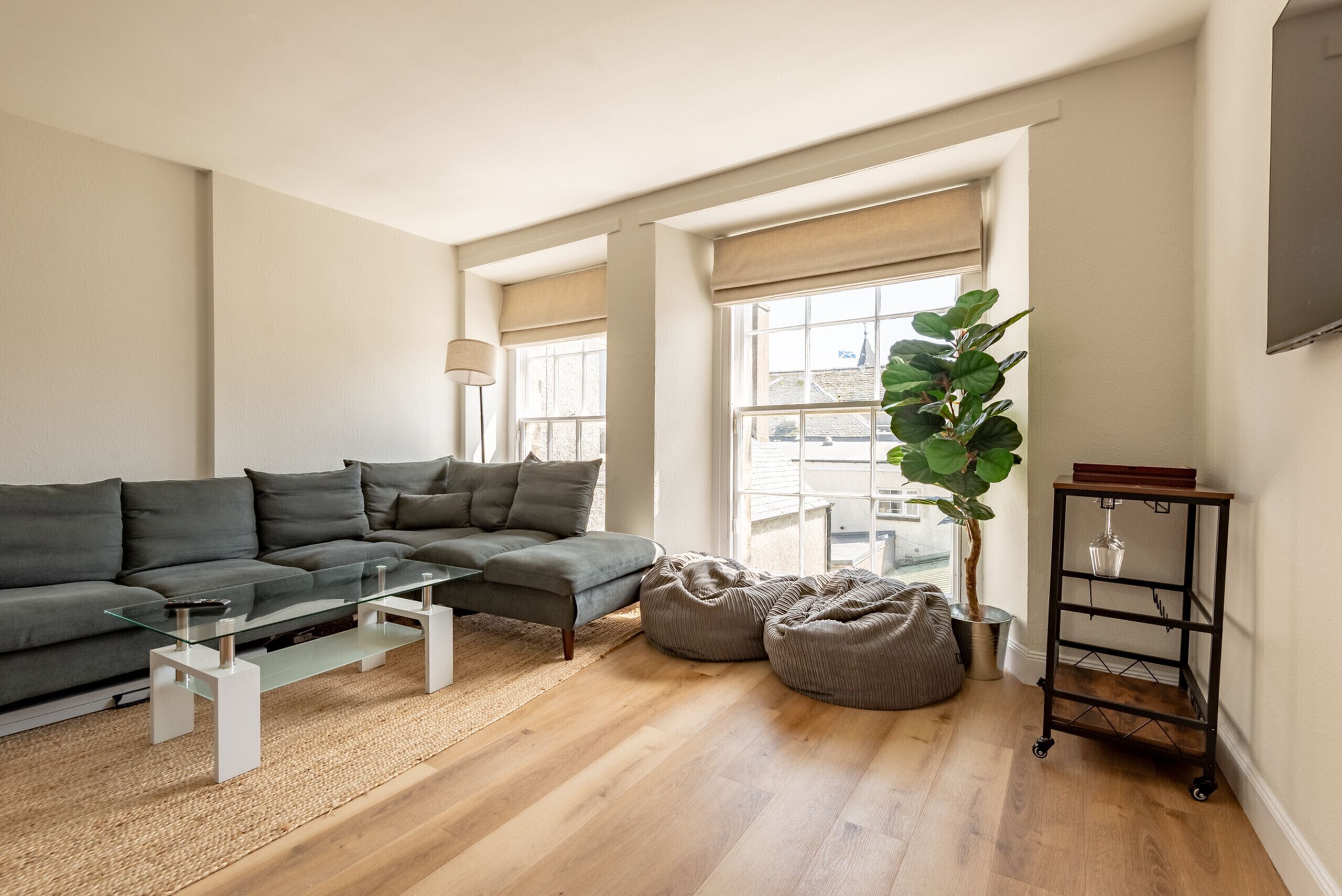 A modern living room with a sectional sofa, a glass coffee table, a bean bag, a floor lamp, and a plant.