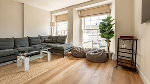 A modern living room with a sectional sofa, a glass coffee table, a bean bag, a floor lamp, and a plant.