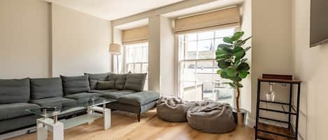 Un salon moderne avec un canapé d’angle, une table basse en verre, un fauteuil poire, une lampe sur pied et une plante.