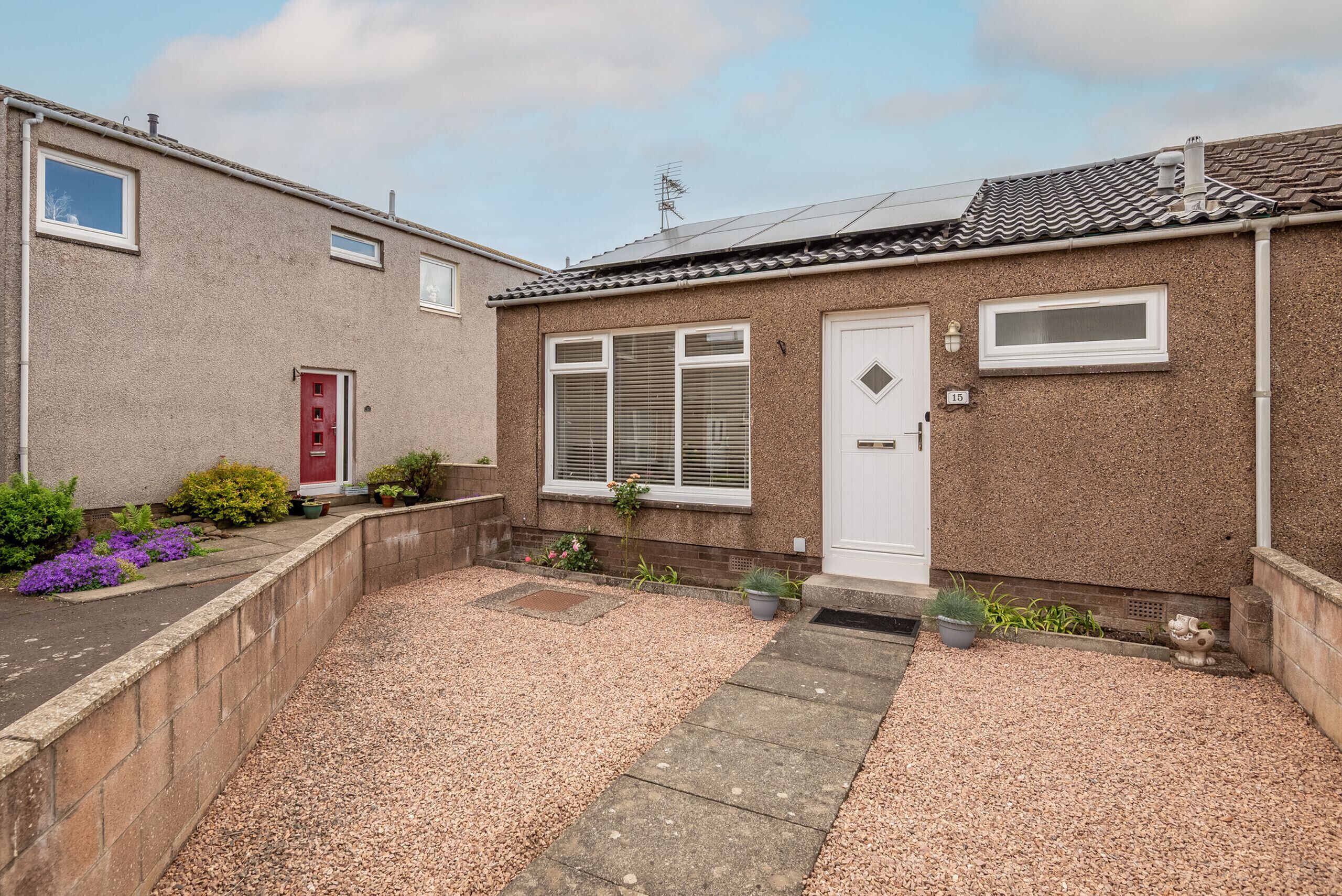 A residential property with a gravel driveway, a red door, and a small garden with various plants.