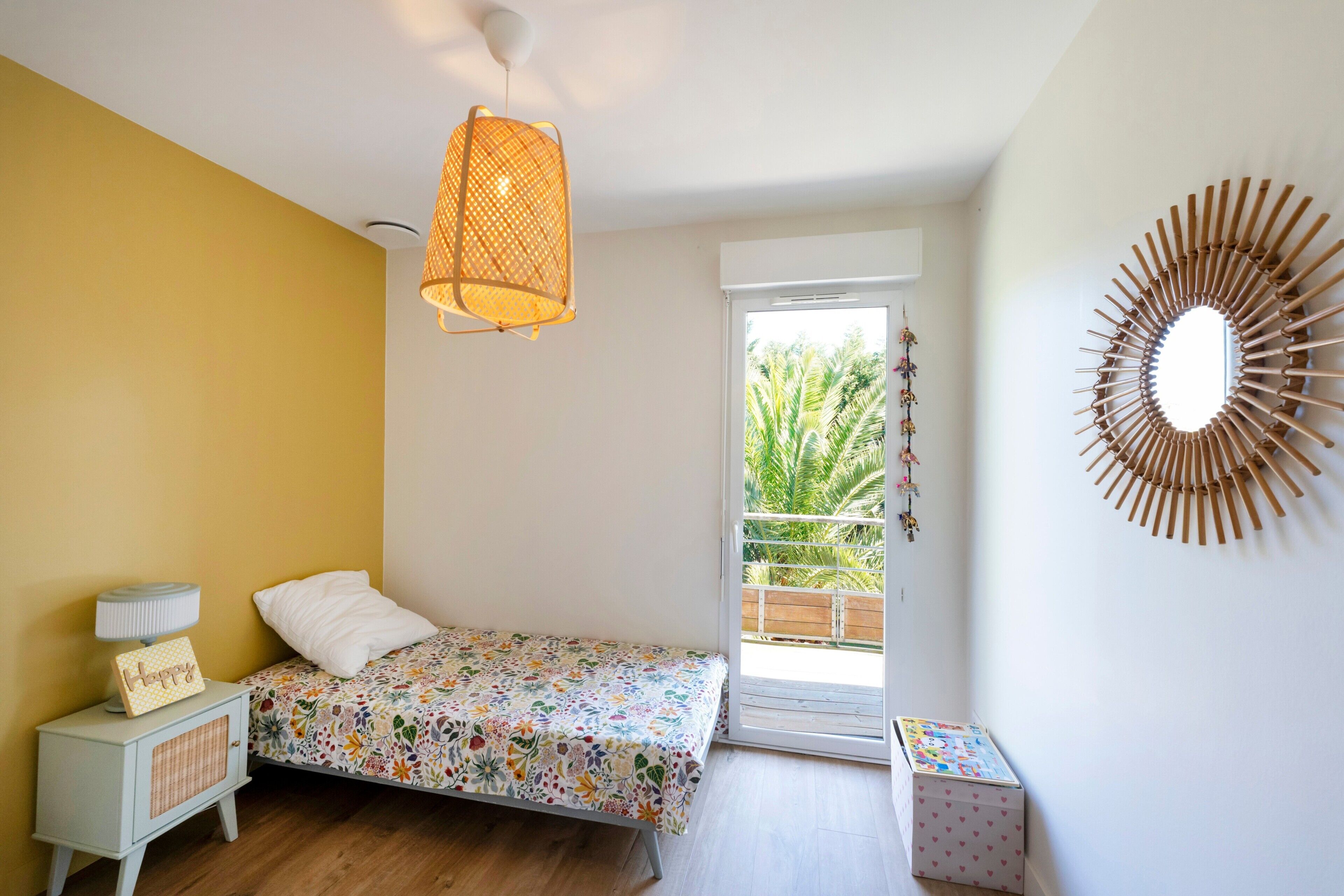 A bedroom with a bed, a nightstand, a lamp, a mirror, and a view of a balcony.