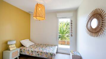 A bedroom with a bed, a nightstand, a lamp, a mirror, and a view of a balcony.