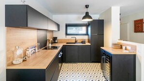 A modern kitchen with a central island, dark cabinetry, a window with blinds, and a patterned floor. - Holiday Home 'Maison De Vacances Oceanides' with Private Terrace, Wi-Fi and Air Conditioning (Capbreton)